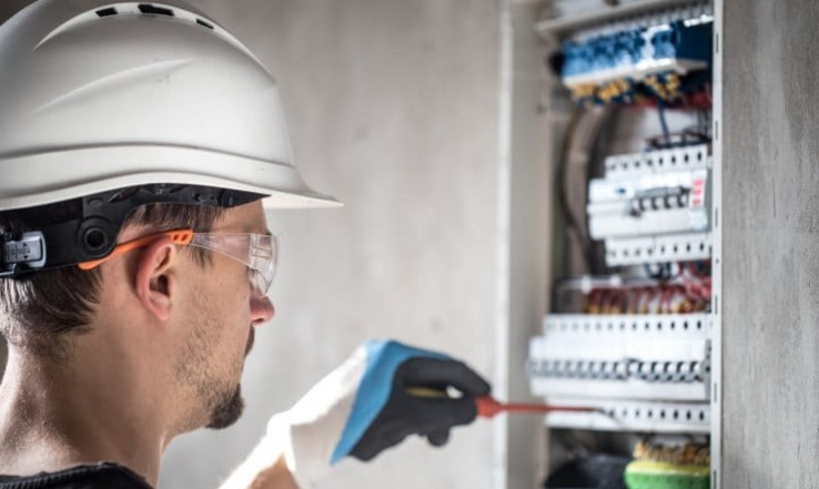 Person wearing hardhat and standing in front of an electrical panel